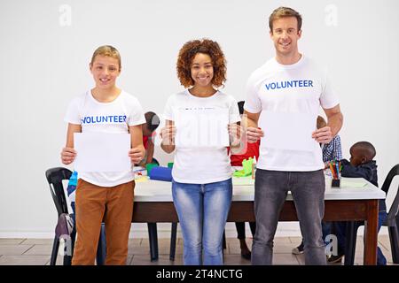 Aider est sa propre récompense. Portrait de bénévoles tenant un panneau vierge tout en travaillant avec de petits enfants. Banque D'Images