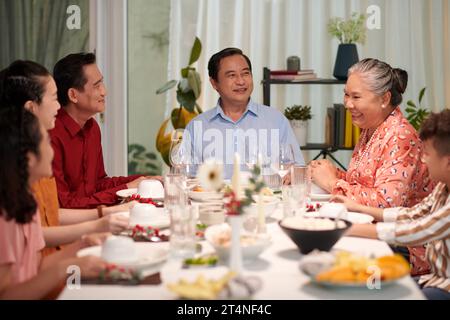Heureuse famille vietnamienne qui parle à une grande table à dîner lorsqu'elle est réunie pour célébrer les vacances Banque D'Images