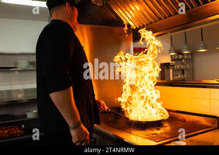 Chef masculin caucasien cuisinant avec poêle avec feu dans la cuisine du restaurant, espace de copie Banque D'Images