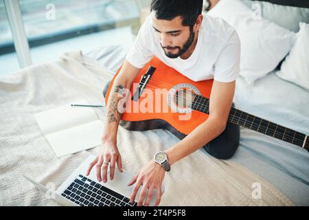 Im prendre des leçons virtuelles pour en savoir plus sur le jeu de la guitare. un homme utilisant son ordinateur portable tout en jouant de la guitare à la maison. Banque D'Images