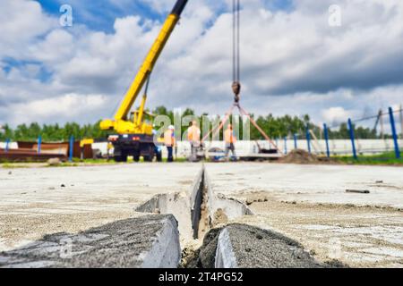 Les constructeurs dans les casques de sécurité travaillent sur le chantier de construction. L'équipe de travailleurs pose la dalle de béton sur le sol le jour de l'été. De vrais travailleurs. Contexte. Banque D'Images