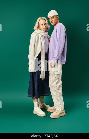 pleine longueur de grand homme élégant debout avec femme blonde en tenue d'hiver sur fond turquoise Banque D'Images