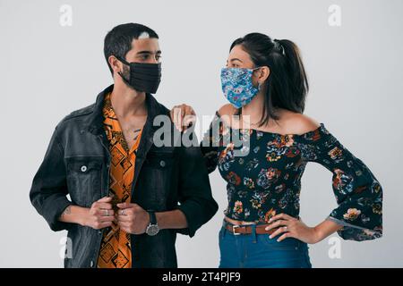 Les masques viennent d'améliorer notre jeu de mode. Photo en studio d'un jeune homme et d'une femme masqués posant sur un fond gris. Banque D'Images