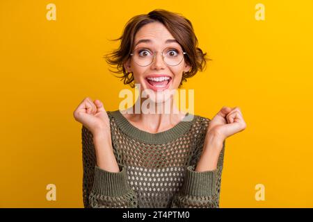 Photo portrait de jolie jeune fille soulève les poings excités porter tricot tendance tenue kaki isolé sur fond de couleur jaune Banque D'Images