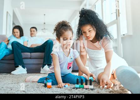 Dis-leur de garder les poupées. deux sœurs jouant sur le sol pendant que leurs parents se détendent en arrière-plan. Banque D'Images