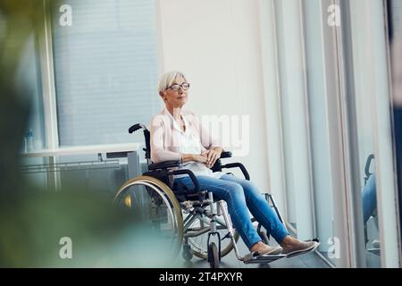 Autant de pages de souvenirs à rallumer. Photo en pied d'une femme âgée qui semble réfléchie alors qu'elle était assise dans son fauteuil roulant dans une maison de retraite. Banque D'Images