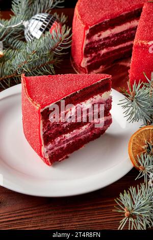 Tranche de Noël festif gâteau de velours rouge sur plaque blanche sur table en bois avec branche de sapin. Banque D'Images