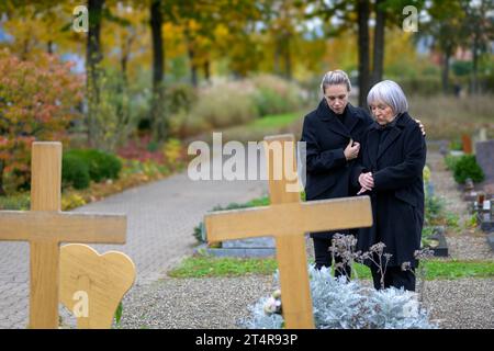 Mère et fille debout à la tombe de l'homme dans le cimetière au premier plan deux croix de bois Banque D'Images