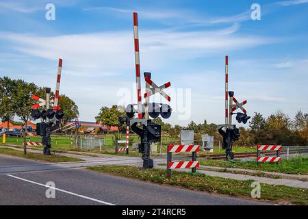 Passage à niveau sur une route rurale, panneau d'arrêt et feux d'avertissement, barrières de passage surélevées, fermes et campagne néerlandaise en arrière-plan, journée ensoleillée d'automne Banque D'Images