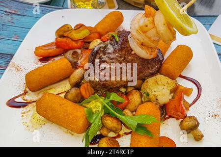 Steak aux crevettes accompagné de légumes sautés et croquettes, baigné d'huile d'olive et sauce soja trempée, garni d'une tranche de citron, servi o Banque D'Images