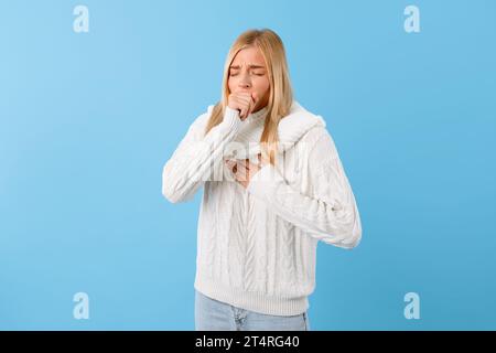 Jeune femme en détresse en chandail toussant, fond bleu Banque D'Images