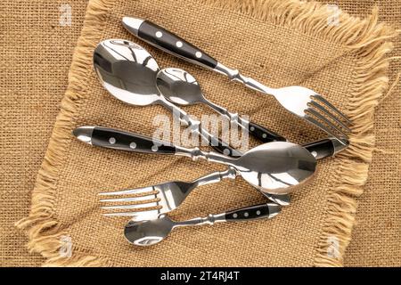 Plusieurs cuillères et fourchettes en métal sur une serviette en jute, macro, vue de dessus. Banque D'Images