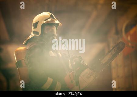 Portrait de pompier portant un équipement complet, un masque à oxygène et une tronçonneuse. Fumée et camions de pompiers en arrière-plan. Banque D'Images