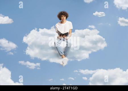 Jeune homme aux cheveux bouclés assis sur un nuage et tenant un livre ouvert Banque D'Images