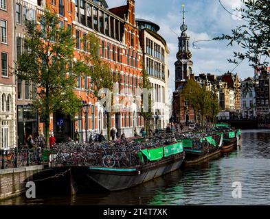 Vue panoramique sur le canal d'Amsterdam avec des vélos garés le long du pont, des bâtiments historiques et des péniches pleines de vélos Banque D'Images