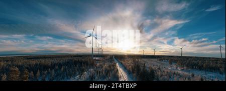 Photo aérienne panoramique au-dessus de la route d'hiver forestière avec des moulins à vent debout en rangée sur le côté gauche dans la forêt. Route au milieu de la vue. Banque D'Images