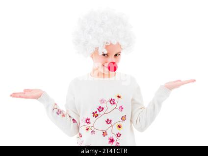 Mignonne adolescente en perruque de clown blanc et grand nez rouge montrant deux paumes vides et regardant la caméra isolée sur fond blanc. CopySpace Banque D'Images