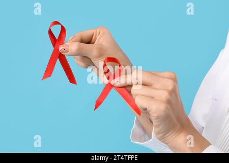 Femme médecin avec des rubans rouges sur fond bleu, gros plan. Concept de la Journée mondiale du sida Banque D'Images