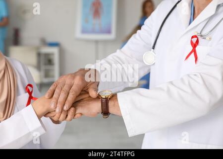 Médecins avec des rubans rouges mettant les mains ensemble dans la clinique, gros plan. Concept de la Journée mondiale du sida Banque D'Images