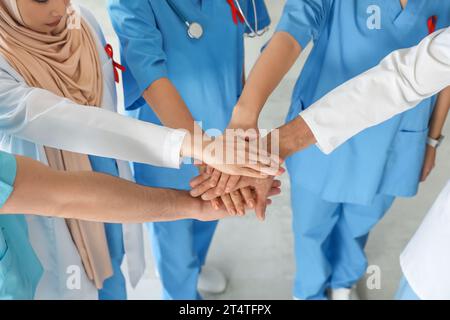 Équipe de médecins avec des rubans rouges mettant les mains ensemble dans la clinique, gros plan. Concept de la Journée mondiale du sida Banque D'Images