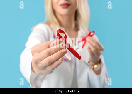 Jeune femme médecin avec des rubans rouges sur fond bleu, gros plan. Concept de la Journée mondiale du sida Banque D'Images