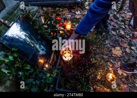 Une femme allume une bougie au cimetière de Rakowicki. La Toussaint en Pologne est une fête familiale très traditionnelle. Les foules visitent des cimetières dans tout le pays pour allumer des bougies et apporter des fleurs aux défunts. Banque D'Images