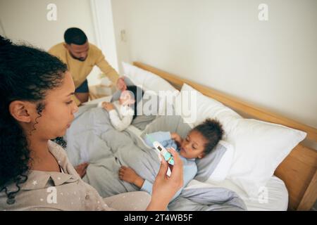 Lit, thermomètre et enfants malades du virus du rhume, de la fièvre ou de la maladie avec une mère inquiète aidant, de l'aide ou du soutien familial. Chambre à coucher à la maison, parents Banque D'Images