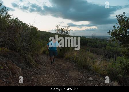 Les hommes en surpoids s'entraînent dans les montagnes soutenus par des bâtons de sport. Banque D'Images