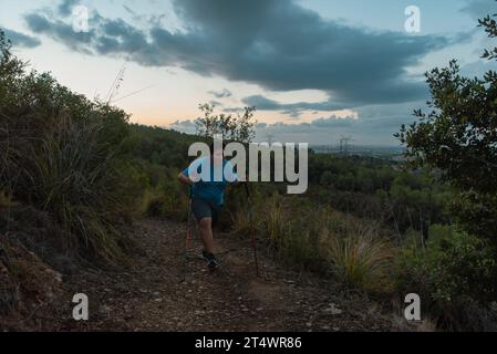 Les hommes en surpoids s'entraînent dans les montagnes soutenus par des bâtons de sport. Banque D'Images