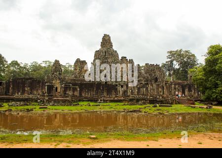 Une photo du temple de Bayon prise de l'entrée nord. Les sculptures de visages sereins sont visibles sur les tours de grès et une statue assise peut l'être Banque D'Images