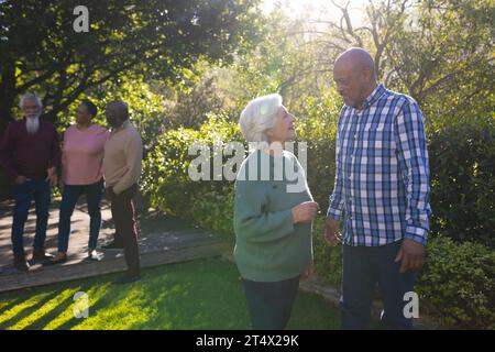 Heureux couple diversifié d'amis seniors embrassant et souriant dans le jardin ensoleillé Banque D'Images