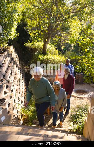 Heureux groupe diversifié d'amis seniors marchant jusqu'aux escaliers dans le jardin ensoleillé Banque D'Images