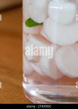 Disques ou tranches de radis Daikon marinés blancs, liquide clair dans un bocal en verre, piment vert pour les épices, goût acidulé de tarte Banque D'Images