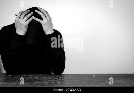 Portrait d'homme déprimé portant un sweat à capuche noir cachant son visage avec les mains. Stressé, désespéré, frustré, trouble mental et cœur brisé. Banque D'Images