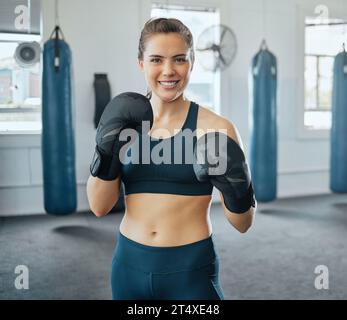 Boxe, combat et gants avec une boxeuse féminine debout dans un club de santé ou une salle de sport. Portrait d'une formation forte et dure jeune femme Banque D'Images