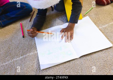 Garçon afro-américain portant un chapeau de noël et dessinant dans un cahier à la maison, espace de copie Banque D'Images