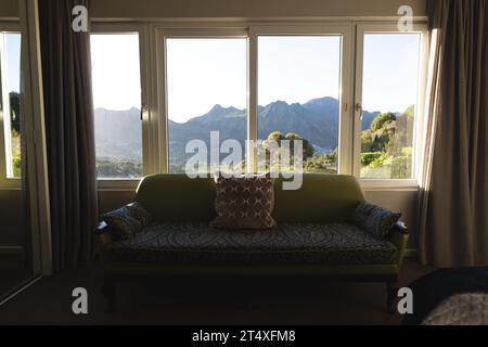 Intérieur de salon domestique ensoleillé avec canapé par fenêtre avec vue sur la montagne, espace de copie Banque D'Images