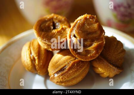 Petits biscuits en forme de noix sur une soucoupe blanche. Deux ouverts en deux. A l'intérieur se trouve un remplisseur de lait condensé. Bonbons sur la table ensoleillée. Banque D'Images