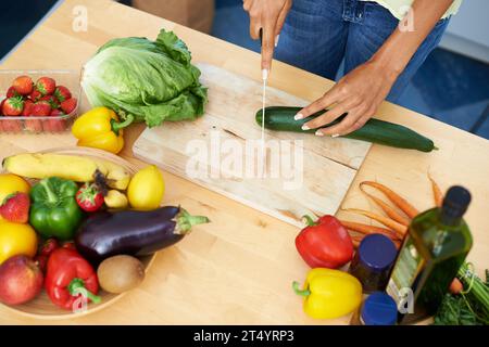 Femme, cuisine et couper le concombre sur une planche de bois ci-dessus pour une alimentation saine ou des légumes à la maison. Vue de dessus des mains de la personne féminine tranchant naturel Banque D'Images