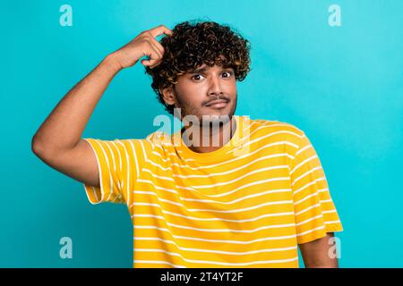 Portrait photo de belle jeune tête de grattage mâle confuse habillé élégant vêtement jaune rayé isolé sur fond de couleur cyan Banque D'Images