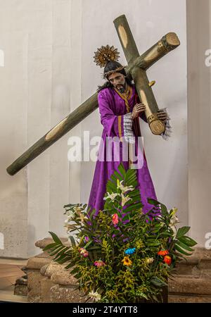 Guatemala, la Antigua - 20 juillet 2023 : Cathédrale de San José. En gros plan, Jésus, en robe violette, portant la statue de la croix. Fleurs à l'avant, beige-blanc W Banque D'Images