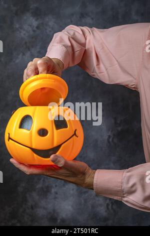 Un homme dans une chemise rose ouvre le couvercle d'un récipient en forme de citrouille d'halloween Banque D'Images