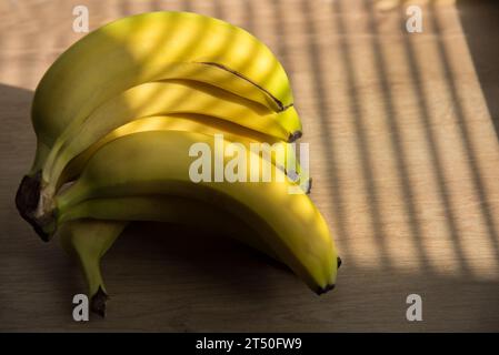 Soleil éclatant à travers les stores de fenêtre et des bandes de coulée sur les bananes et les aplles dans le panier Banque D'Images