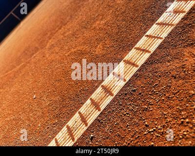 Vue détaillée inhabituelle de la ligne de bordure blanche sur un court de tennis en argile orange. Courts de tennis extérieurs traditionnels Banque D'Images