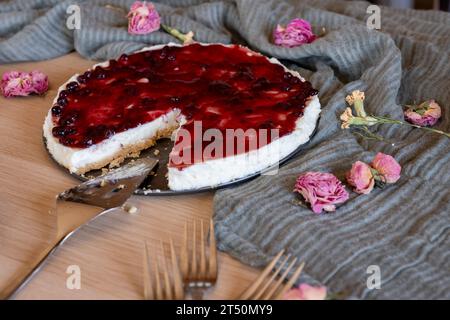 Cheesecake froid avec gelée de cerise servi sur table en bois avec fourchettes fleurs roses et voile vert Banque D'Images