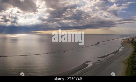 Vue aérienne de la plage de sable et du ciel orageux avec les rayons du soleil perçant les nuages, mer plate à l'aube, Italie Banque D'Images