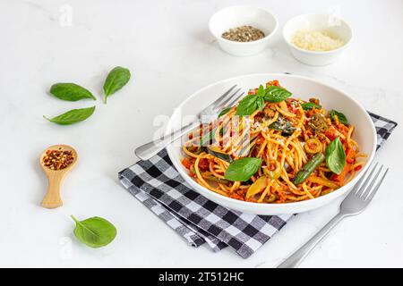 Pâtes Pomodoro garnies de feuilles de basilic frais, d'herbes et de fromage dans un bol sur fond blanc Banque D'Images