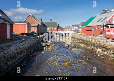 Petit ruisseau de rivière traversant le milieu de la ville de Qaqortoq au Groenland, l'église de notre Sauveur en arrière-plan Banque D'Images