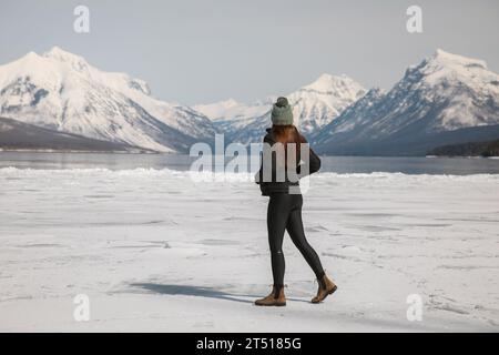 Femme marche sur le lac Frozen dans le parc national Glacier avec des montagnes enneigées au loin- Lake McDonald Banque D'Images