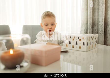 Un garçon prépare des cadeaux pour Noël. Cadeau sur la table. La bougie brûle. Banque D'Images